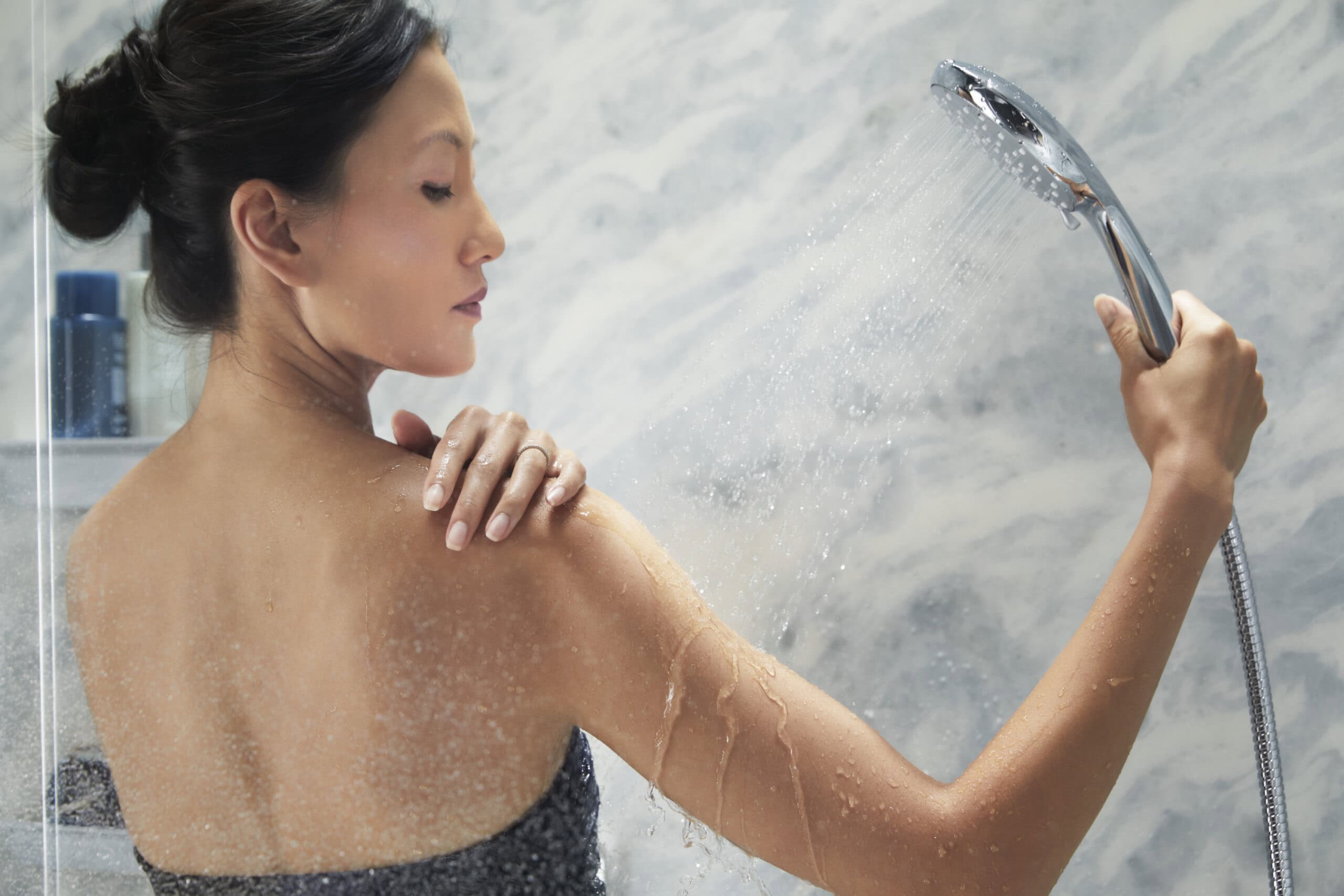 woman showering with handheld showerhead|bath salt|bath towels|essential oils